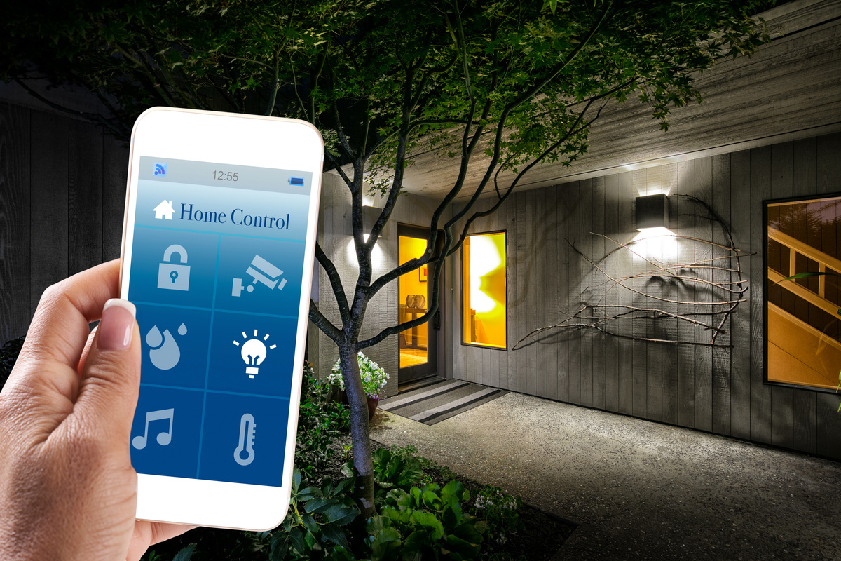 Home Automation: Woman holding Smart Home app with smart phone in living room of house. Concept for home automation